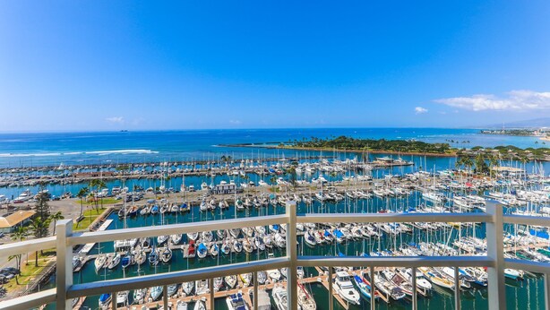A marina with numerous boats docked, surrounded by clear blue water and a distant shoreline. - Ilikai Marina #1780, Beautiful Ocean, Sunset and Harbor views! (Honolulu)