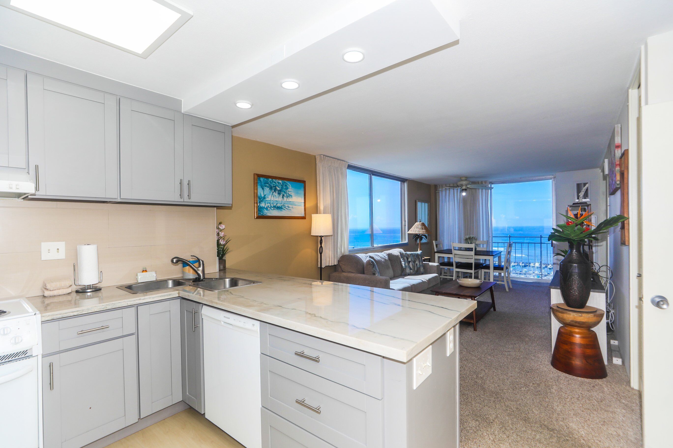 A modern kitchen with white cabinets, a central island, and a dining area with a view of the ocean.
