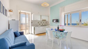 Cozinha moderna com armários brancos, uma mesa de jantar com cadeiras e vista para o mar através de grandes janelas.