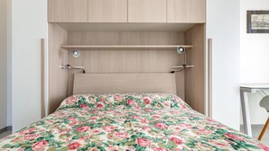 Uma cama com colcha floral, cabeceira de madeira e duas mesas de cabeceira com luminárias.