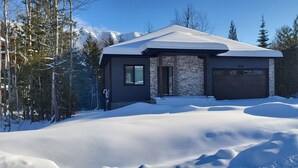 Ein modernes Haus mit Steinverkleidung, einer dunklen Garagentür und einem mit Schnee bedeckten Dach.