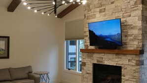 Ein modernes Wohnzimmer mit Kamin aus Stein, einem Wand-Fernseher und einer gemütlichen Sitzecke.
