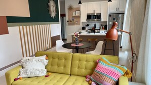 Ein modernes Wohnzimmer mit einem gelben Sofa, einem Couchtisch und einer Küche im Hintergrund.