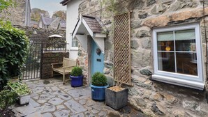 A stone building with a blue door, a wooden bench, and potted plants. - 3 Ivy Court (Dolgellau)