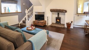 A cozy living room with a fireplace, wooden flooring, and a staircase leading to an upper level. - 3 Ivy Court (Dolgellau)