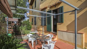 An outdoor patio with a round table and chairs, a small garden area, and a building with green shutters. - Casa Bellesi - Sweet Dreams in Florence (Firenze)