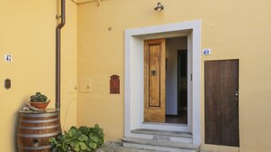 A yellow building with a wooden door, a number 49 sign, a barrel, and a potted plant. - Casa Bellesi - Sweet Dreams in Florence (Firenze)