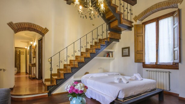 A bedroom with a double bed, a wooden staircase, and a chandelier. - Casa Bellesi - Sweet Dreams in Florence (Firenze)