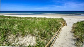 Un sentier de sable bordé de chaque côté d’herbe, qui mène à l’océan.