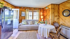 A cozy cabin interior with a wooden interior, a sofa, a dining table, and a refrigerator.