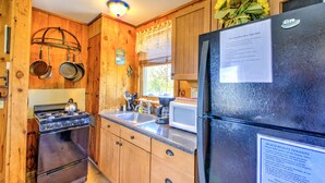 A kitchen with wooden cabinets, a stove, a sink, and a refrigerator. There is a sign on the refrigerator and a window with blinds.