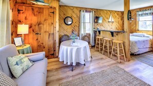 A cozy room with a wooden wall, a round table with chairs, a sofa, and a bed.