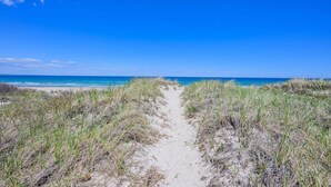 Ein sandiger Pfad führt zu einem Strand unter blauem Himmel.
