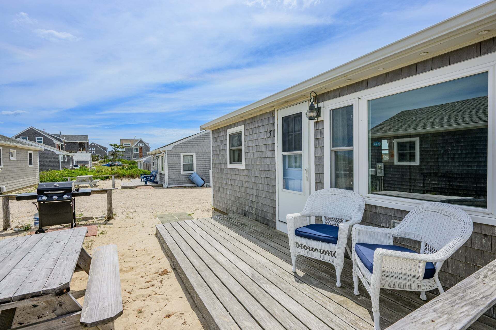 Une terrasse au bord de la plage, aménagée avec du mobilier d’extérieur, un barbecue et offrant une vue sur les maisons voisines.