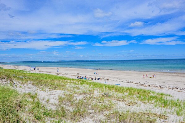 A beach with sand, grass, and a clear sky.