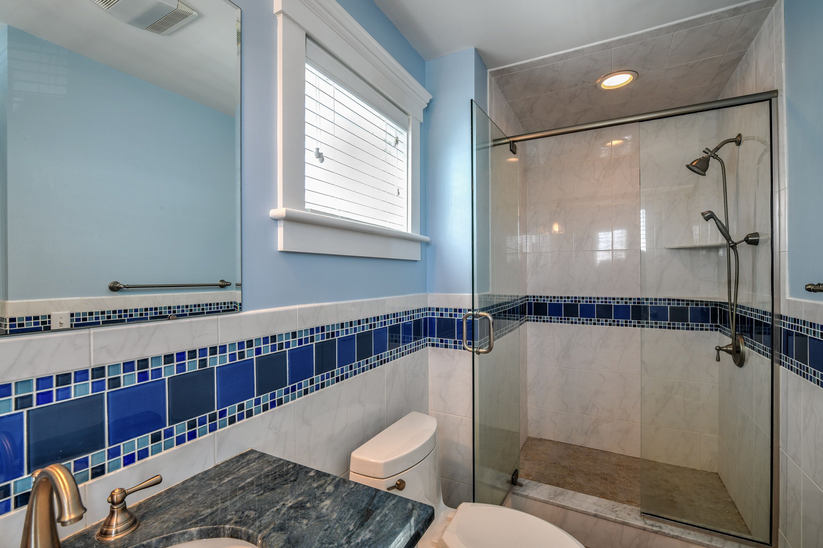 A bathroom with a glass shower enclosure, a toilet, and a sink with a marble countertop.