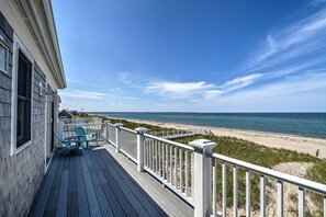Eine Holzterrasse mit Stühlen und Geländer mit Blick auf einen Strand.