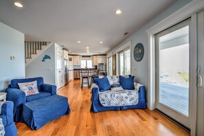 Un vaste espace de vie avec deux canapés bleus et des poufs, un plancher en bois et une cuisine à l’arrière-plan.