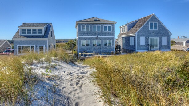 Ein Küstenhaus mit einem Sandweg, der davorführt, umgeben von hohem Gras.