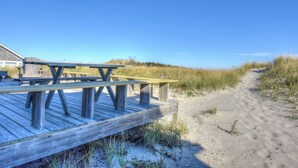 Eine Holzterrasse mit Picknicktischen, die zu einem Sandstrand führt.