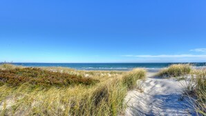 Ein Küstenpfad mit Sand und Gras, der zum Meer unter blauem Himmel führt.