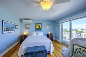 A bedroom with a bed, a nightstand, a dresser, a window with a view, and a ceiling fan.