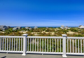 Uitzicht op de kust vanaf een balkon met een witte reling, uitkijkend op een zandstrand en verschillende huizen.