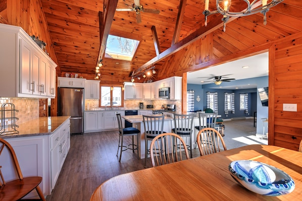 A spacious kitchen with wooden beams, white cabinets, and a large island with bar stools.