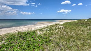 A beach with a dune and a small structure in the distance. - Beachside Bliss with Skylights & Fireplace (East Sandwich)