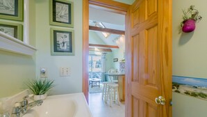 A bathroom with a large bathtub, a sink, and a mirror. There are framed pictures on the wall and a potted plant on the counter. - Beachside Bliss with Skylights & Fireplace (East Sandwich)