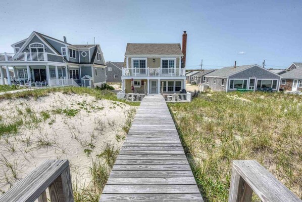 A wooden boardwalk leading to a house with a porch and multiple windows.