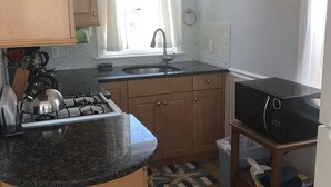 A kitchen with a gas stove, sink, wooden cabinets, a microwave, and a small stool. - Oceanfront Cottage—Private Beach & Bay Views (East Sandwich)