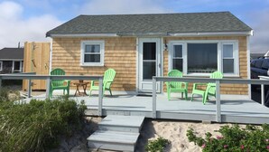 A wooden house with a porch, green chairs, and a small table. - Oceanfront Cottage—Private Beach & Bay Views (East Sandwich)