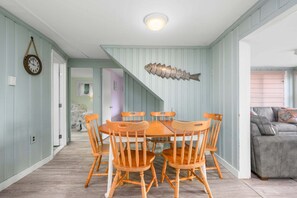Un coin repas avec une table et des chaises en bois, un élément décoratif mural en forme de poisson et un escalier menant à une autre pièce.