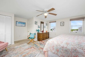 Ein Schlafzimmer mit einem Bett, einem Deckenventilator, einem Schminktisch, einem Stuhl und einem Fenster mit Blick.