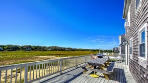 Eine Holzterrasse mit Picknicktisch und Stühlen mit Blick auf einen Strand und eine Wiese.