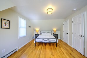 Une chambre à coucher avec un lit, deux tables de chevet avec des lampes, une fenêtre avec des stores et une porte.