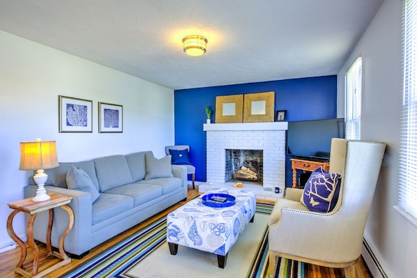 Un salon avec un mur d’accent bleu, une cheminée blanche, un canapé, une table basse et un fauteuil.