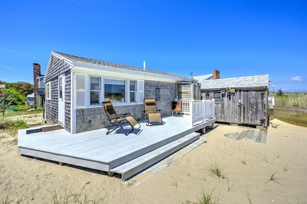 A beach house with a deck, outdoor seating, and a small shed.