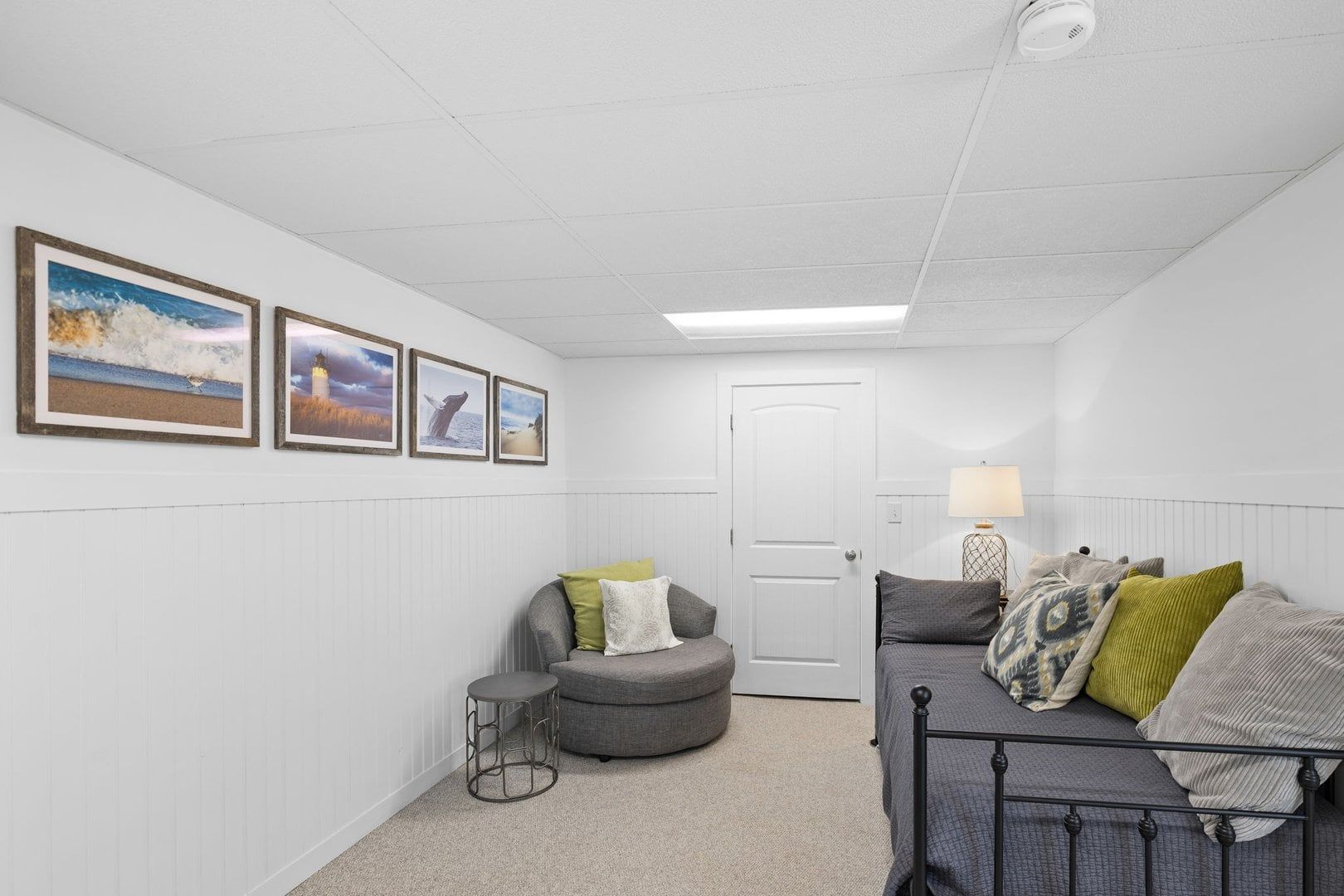 A room with a bed, a chair, a lamp, and framed pictures on the wall.