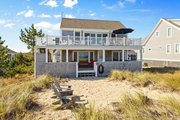 A two-story beach house with a balcony, a covered porch, and a sandy front yard. - Oceanfront at Sagamore Beach (Sagamore Beach)