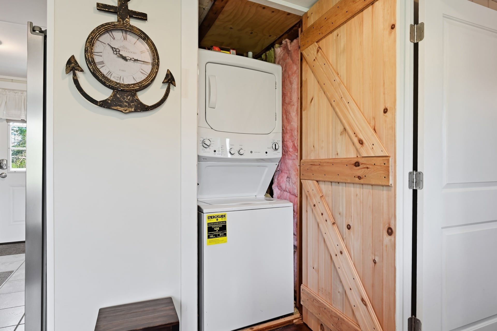 Een wasserette met een klok aan de muur, een gestapelde wasmachine en droger, en een houten deur.