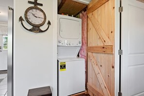 Une buanderie avec une horloge fixée au mur, un lave-linge et un sèche-linge superposés, et une porte en bois.