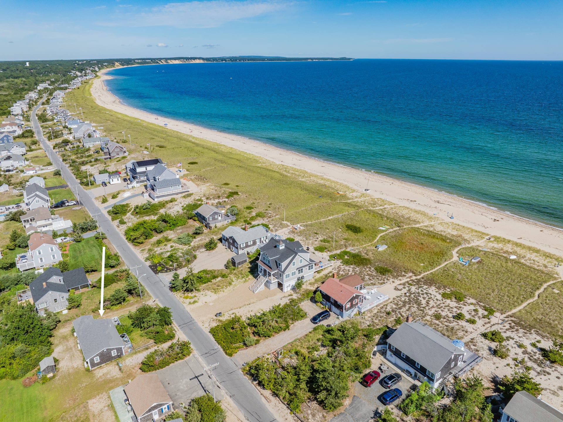 Área residencial costeira com casas ao longo da praia, uma avenida principal e vista clara do oceano.