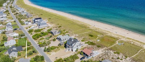 A coastal residential area with houses along a beachfront, a main road, and a clear view of the ocean.