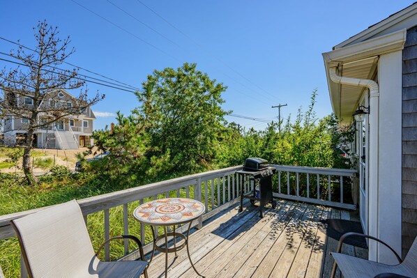 Une terrasse en bois avec une table et des chaises décorées de motifs en mosaïque, un barbecue et une vue sur les maisons et les arbres des environs.