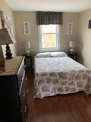 Um quarto com uma cama, duas mesas de cabeceira com abajures, um penteado, uma janela com cortinas e quadros nas paredes.