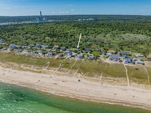 Eine Luftaufnahme einer Küstenwohngegend mit Häusern, einem Strand und einer in der Ferne liegenden Industrieanlage.