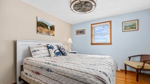 Ein Schlafzimmer mit einem Bett, einem Nachttisch, einem Sessel und drei gerahmten Bildern an der Wand.