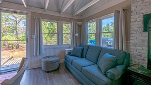 Ein Zimmer mit einer Couch, Hocker und Blick ins Freie.
